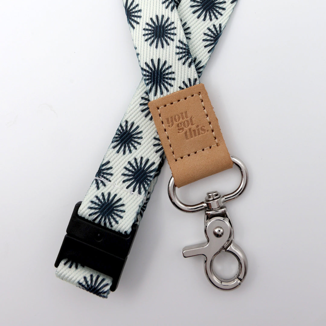 Lanyard with star pattern, brown leather tag, and metal clip on a light gray background