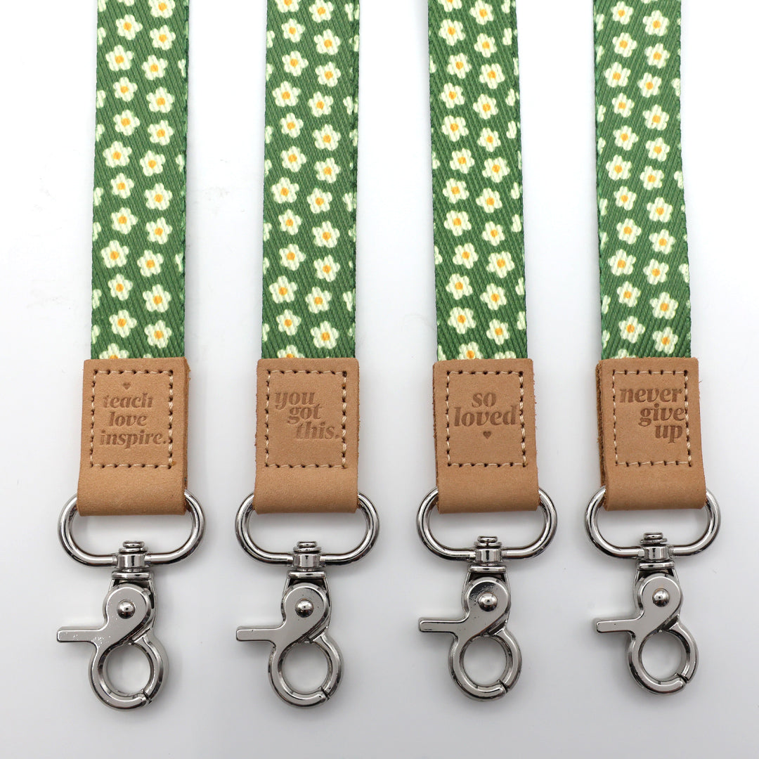 Four green floral patterned straps with brown leather accents and metal clasps on a white background.
