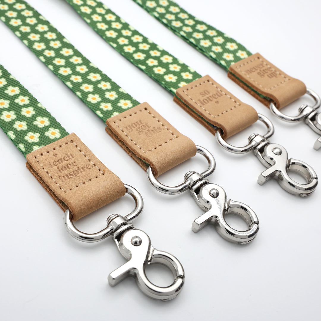 Two green floral-patterned dog leashes with silver clamps and brown leather patches on a white background.