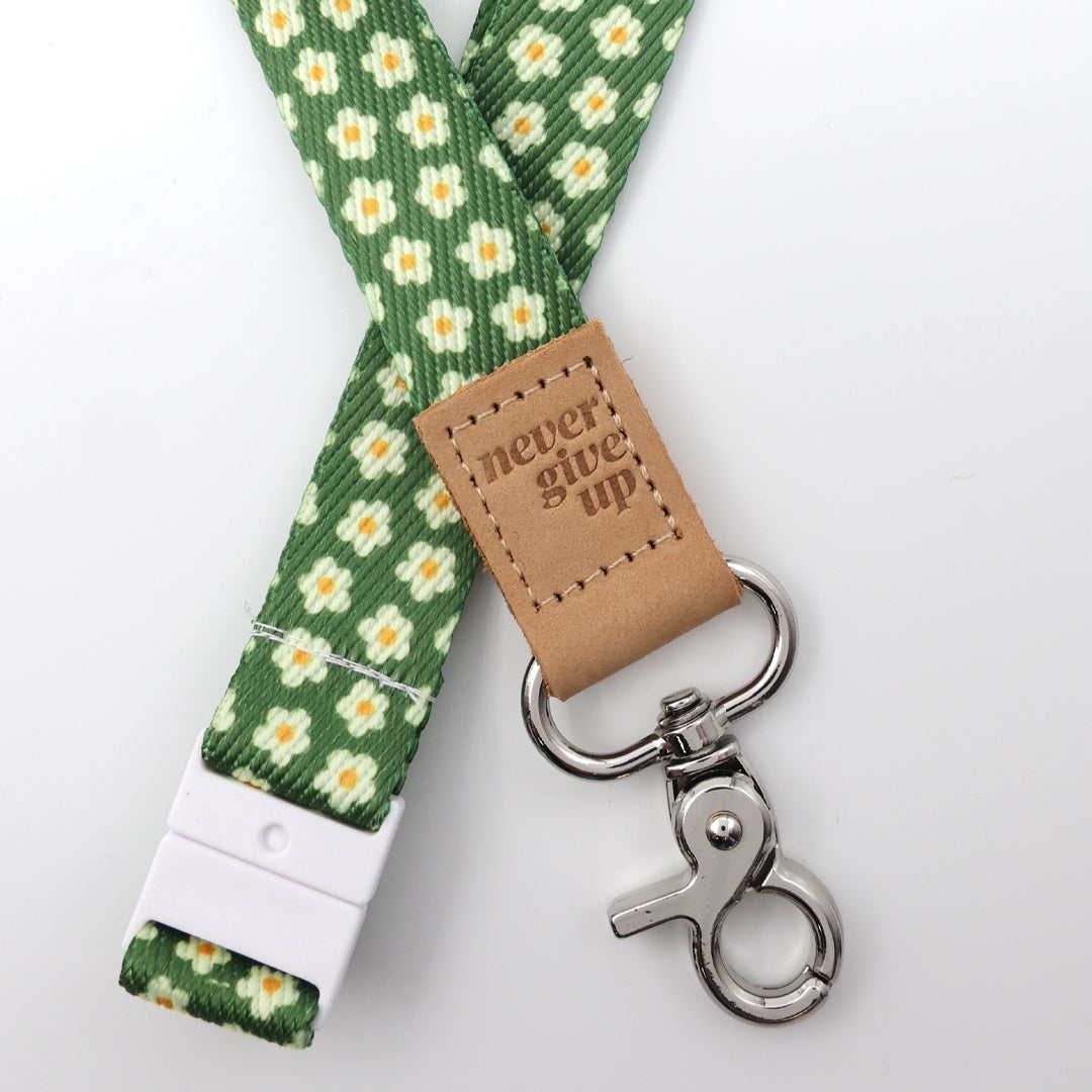 Green floral patterned lanyard with leather tag and metal clip on a white background
