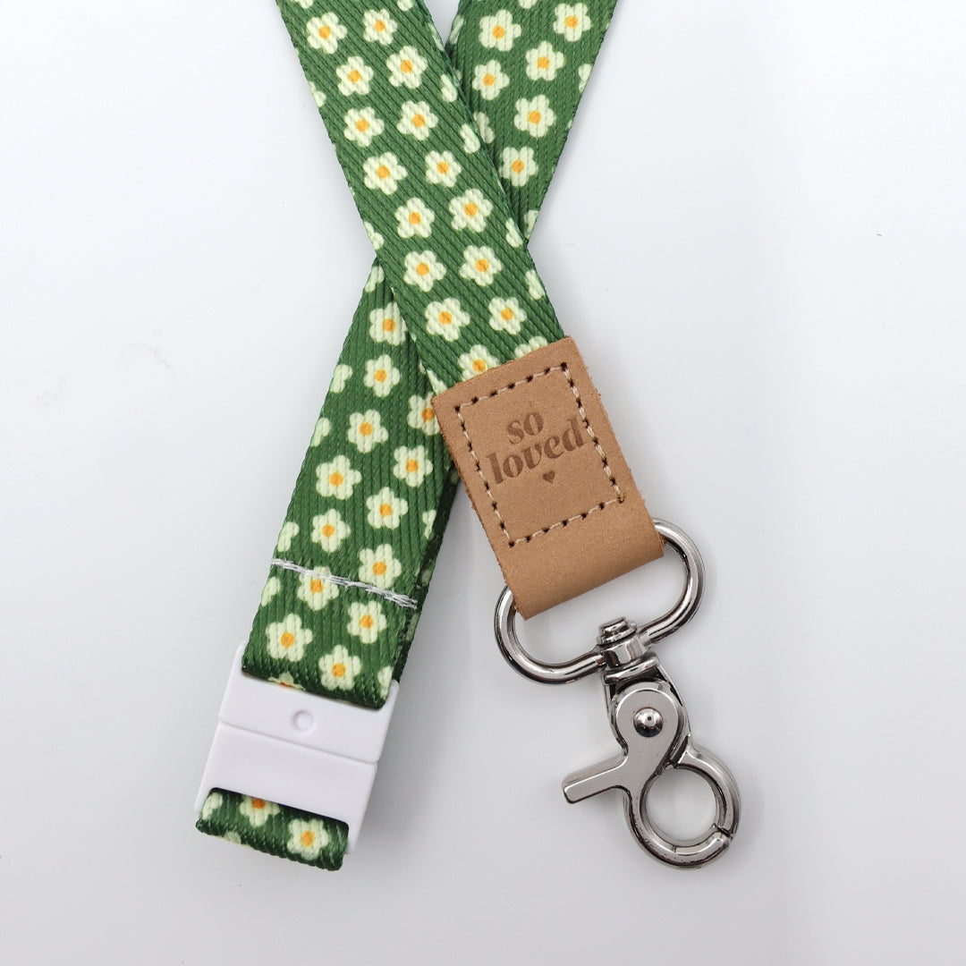 Green floral lanyard with a brown leather tag and metal clip on a white background