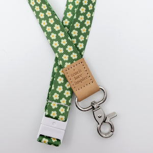 Green floral lanyard with a brown leather tag and metal clip on a white background