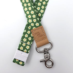 Green floral lanyard with a brown leather tag and metal clip on a white background
