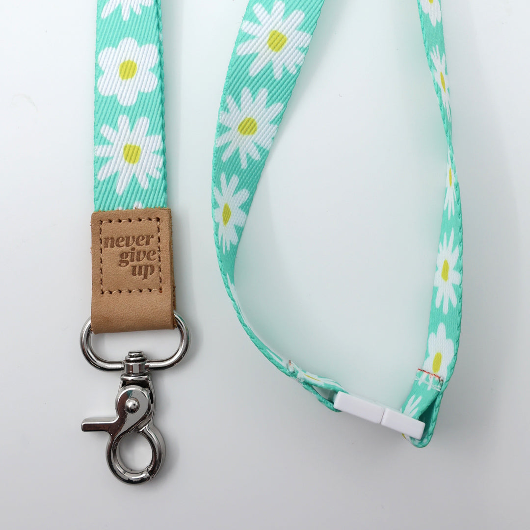 Lanyard with daisy pattern and 'never give up' leather tag on a light gray background