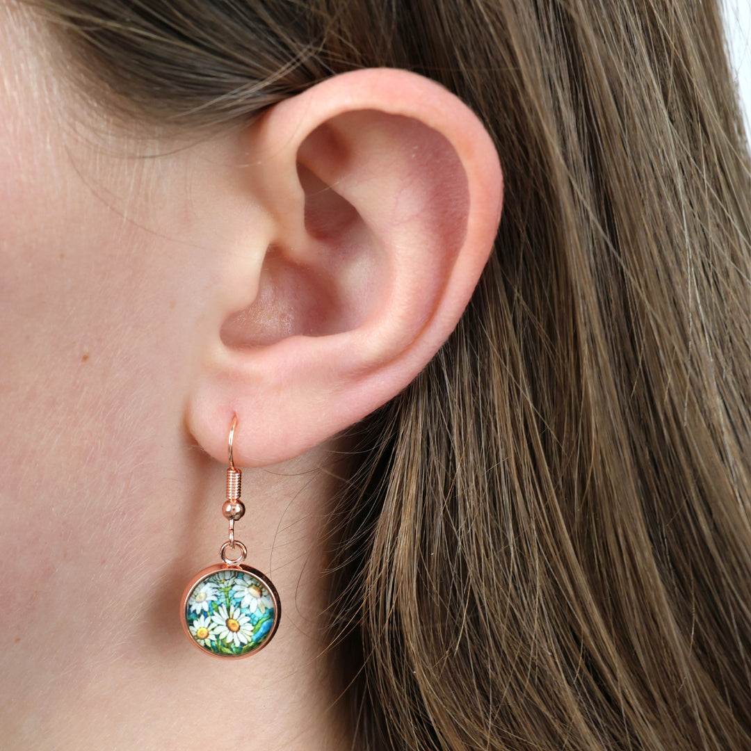 Close-up of an ear wearing a floral earring with greenery and flowers.