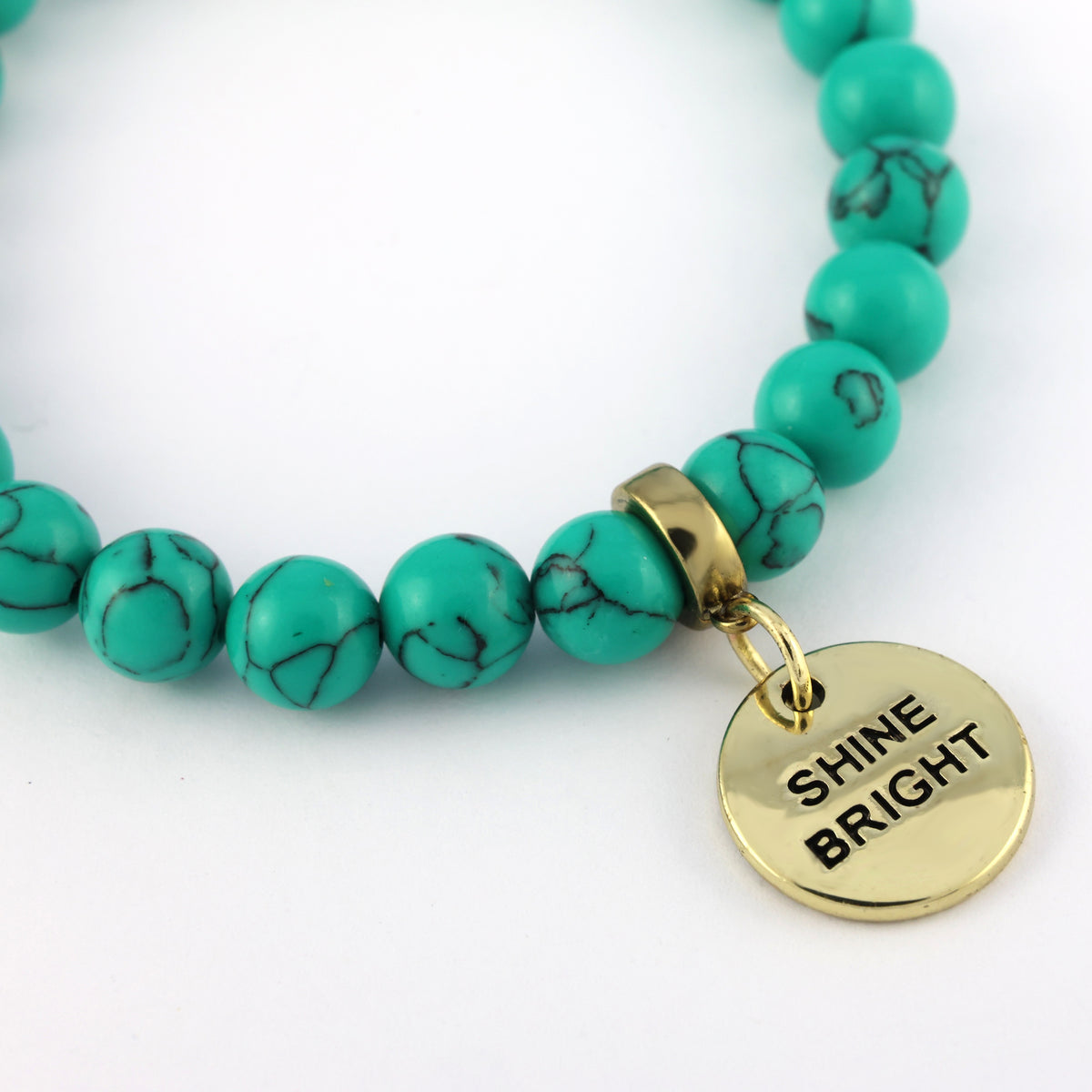 Turquoise beaded bracelet with a gold charm that says 'Shine Bright' on a white background