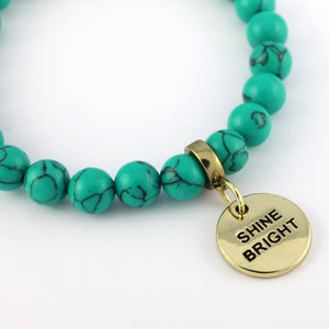 Turquoise beaded bracelet with a gold charm that says 'Shine Bright' on a white background