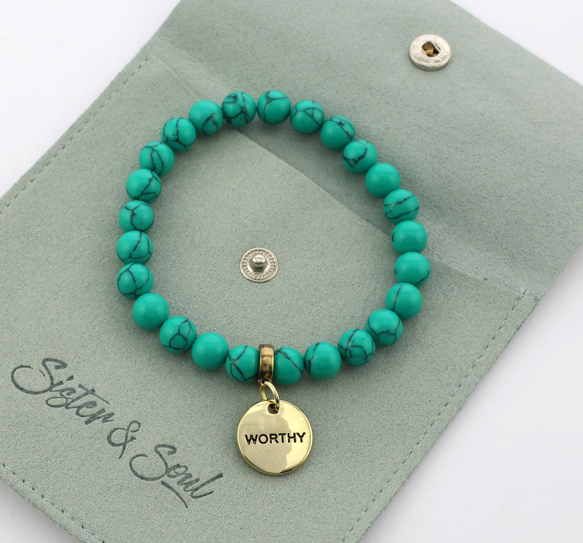Turquoise beaded bracelet with a gold 'WORTHY' charm on a green card with 'Sister & Soul' branding.