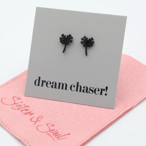 Black earrings on a card with 'dream chaser!' text, placed on a pink surface with 'Sister & Soul' branding.