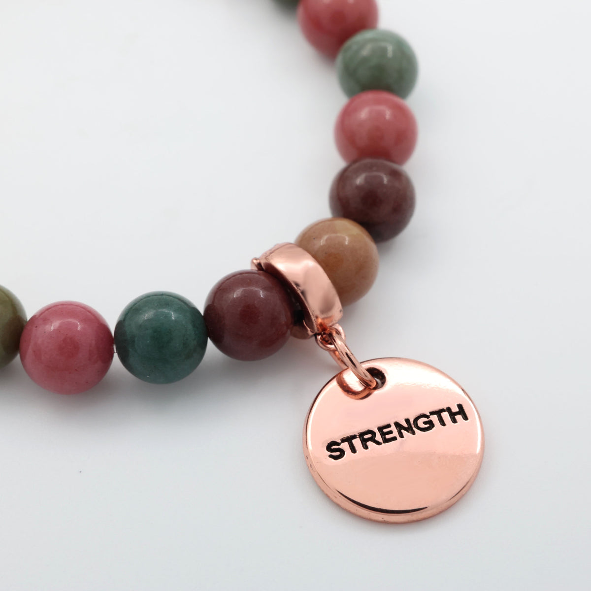 Bracelet with multicolored beads and a rose gold 'STRENGTH' charm on a light background
