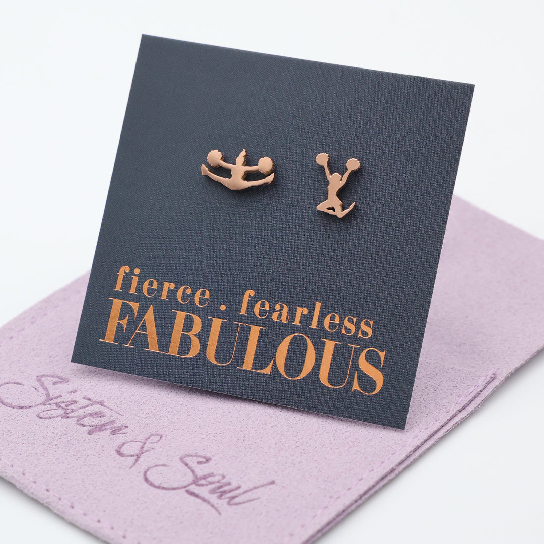 Cheer leader shaped Rose gold earrings on a card with 'fierce fearless FABULOUS' text, placed on a pink surface.