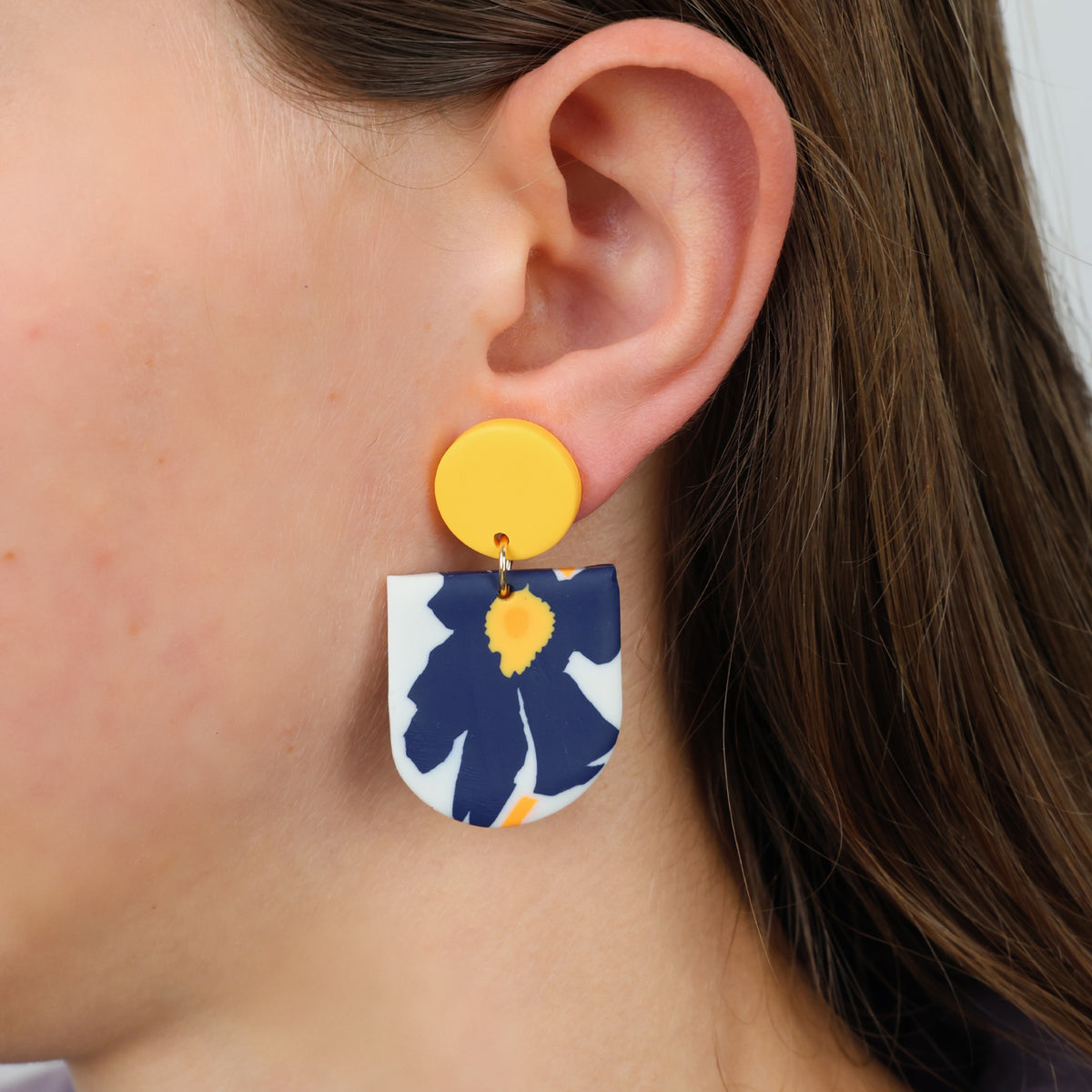 Close-up of a person wearing a floral earring with a yellow center.