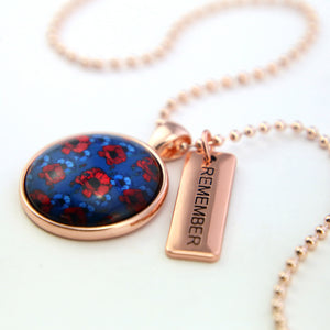 Necklace with a blue floral pendant and 'REMEMBER' tag on a white background