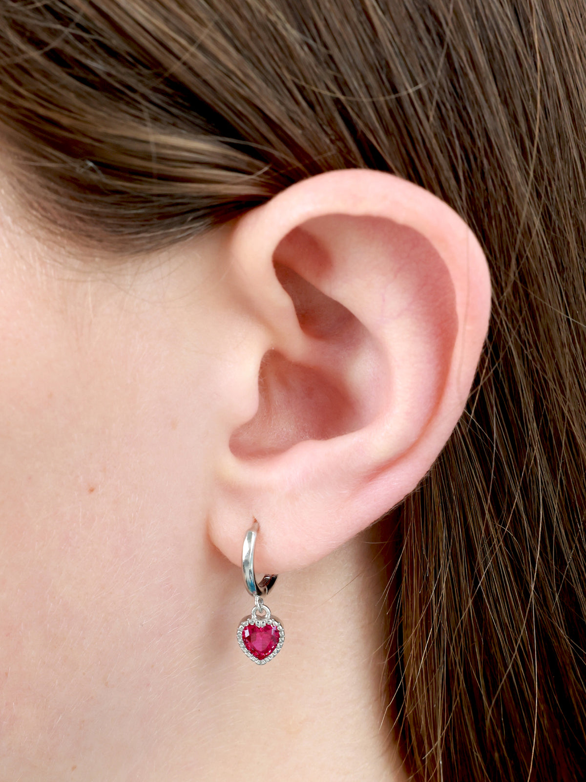 Pink heart shaped silver huggies hoop earrings in a girls ear. 