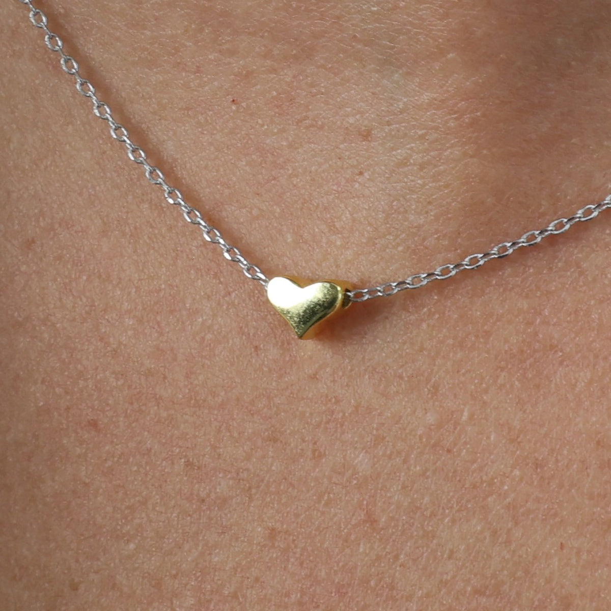 Gold heart-shaped pendant on a silver chain against skin background