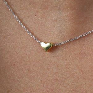 Gold heart-shaped pendant on a silver chain against skin background