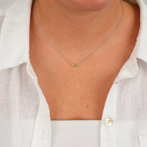 Person wearing a delicate necklace with a heart pendant against a white shirt background