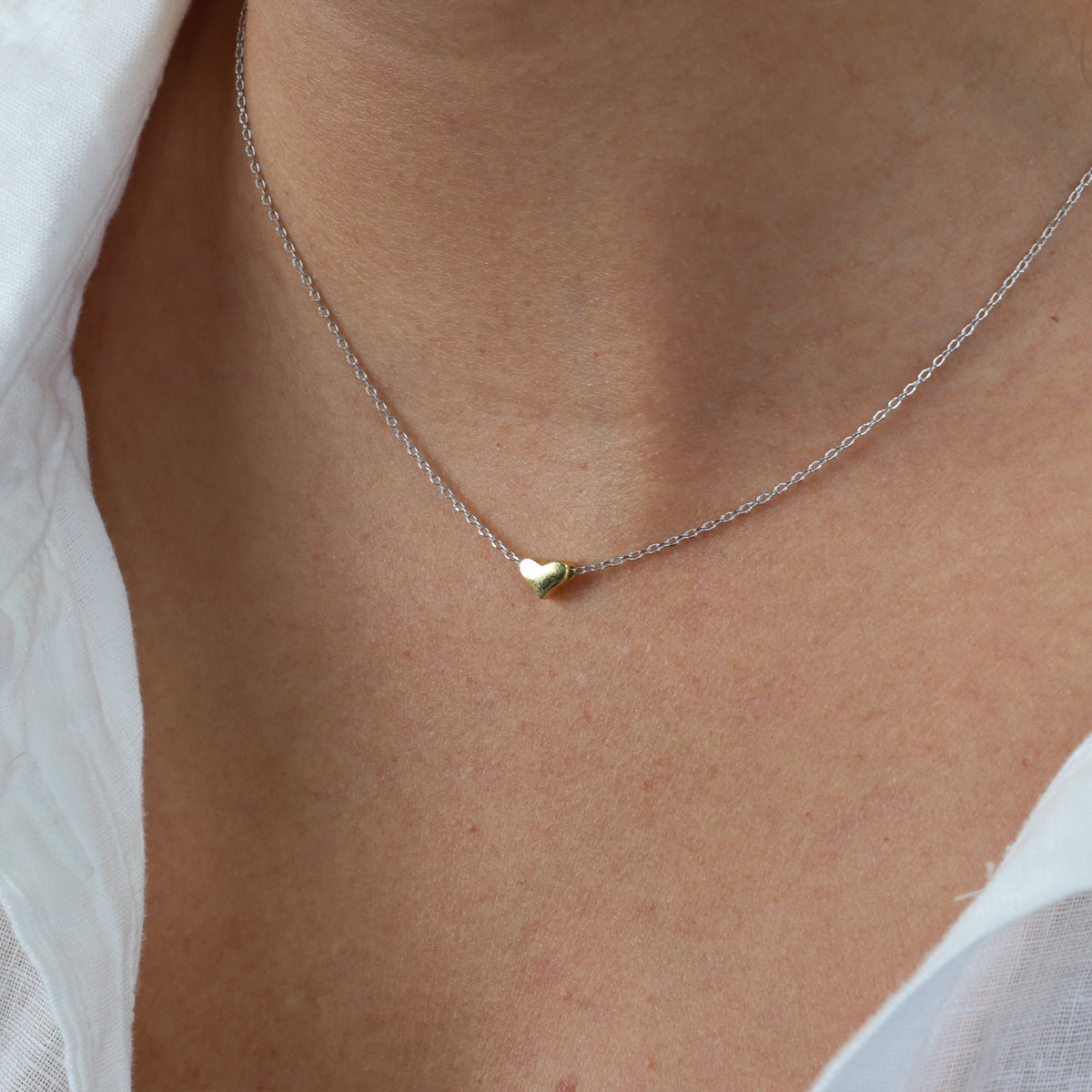 Necklace with a heart-shaped pendant on a person wearing a white shirt.