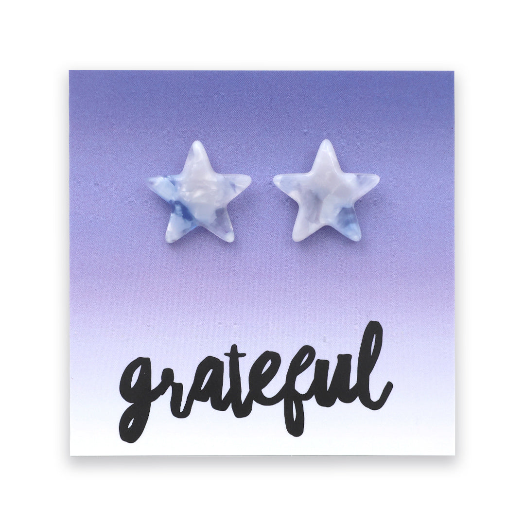 A pair of star-shaped stud earrings with a light blue and white marbled pattern, displayed on a lavender-to-white gradient backing card with the word 'grateful' in black script.