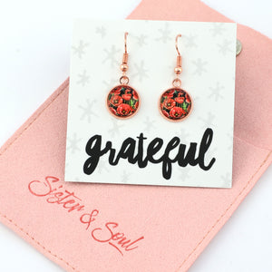 Earrings on a card with 'grateful' text, displayed on a pink fabric background.