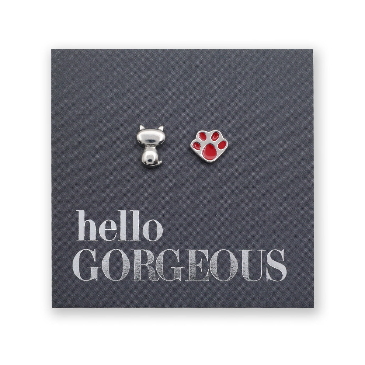 A pair of small stud earrings displayed on a dark gray backing card. One earring is a silver cat-shaped charm, and the other is a red paw print earring.