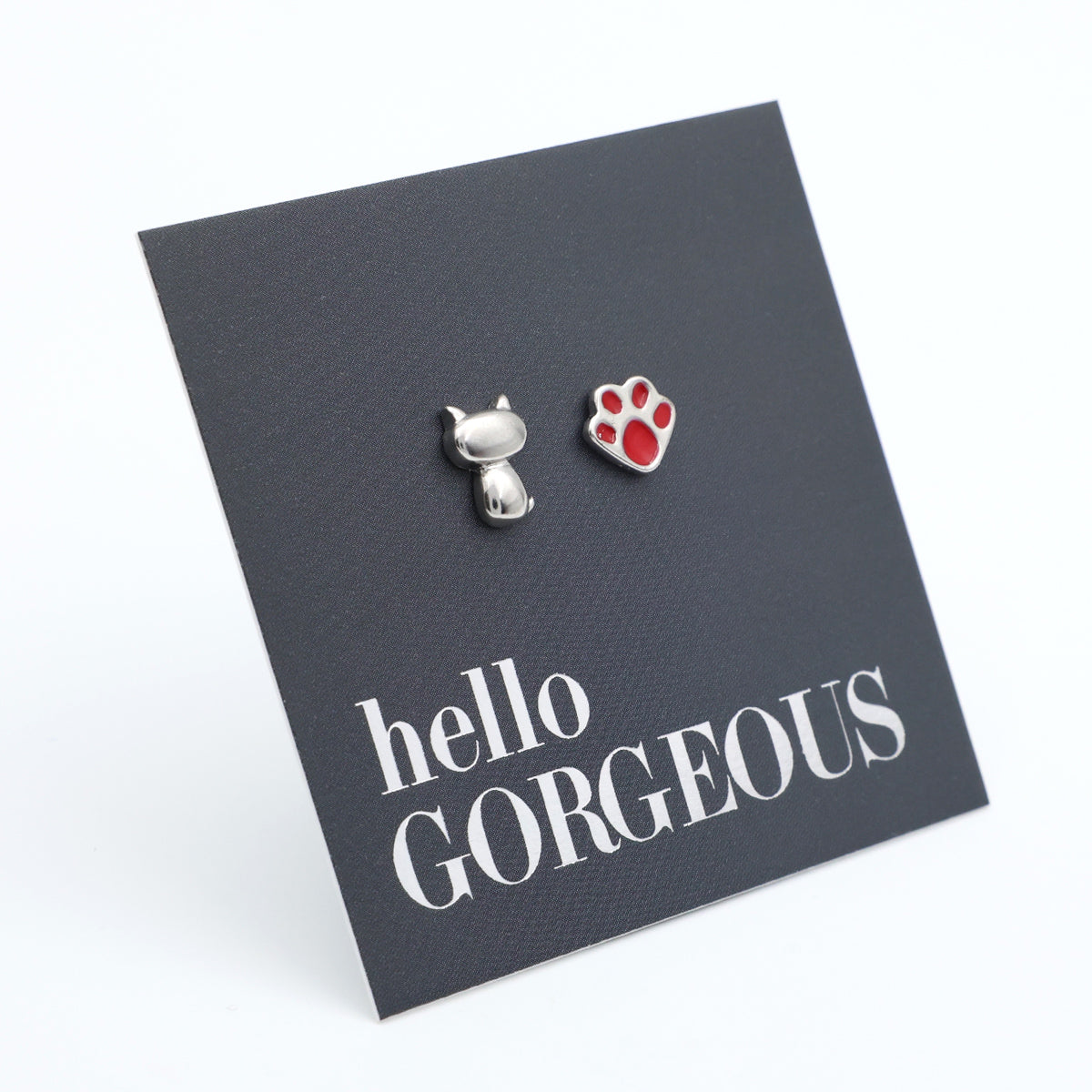 A pair of pet-themed stud earrings on a dark gray display card. One earring is a small silver cat silhouette, and the other is a silver paw print with a red pad.