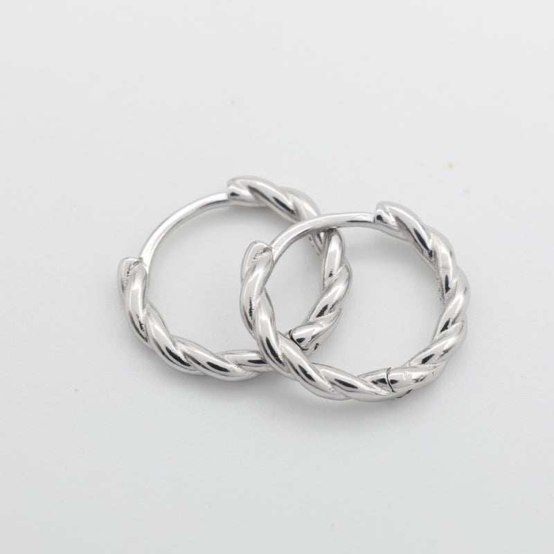 Two silver twisted hoop earrings overlapping on a plain light gray background.