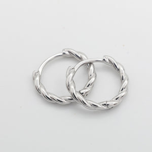 Two silver twisted hoop earrings overlapping on a plain light gray background.