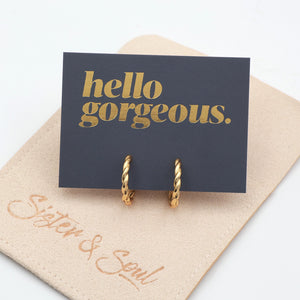 Gold twisty hoops grey card with gold writing "Hello Gorgeous"on top of a beige coloured pouch on a white background 