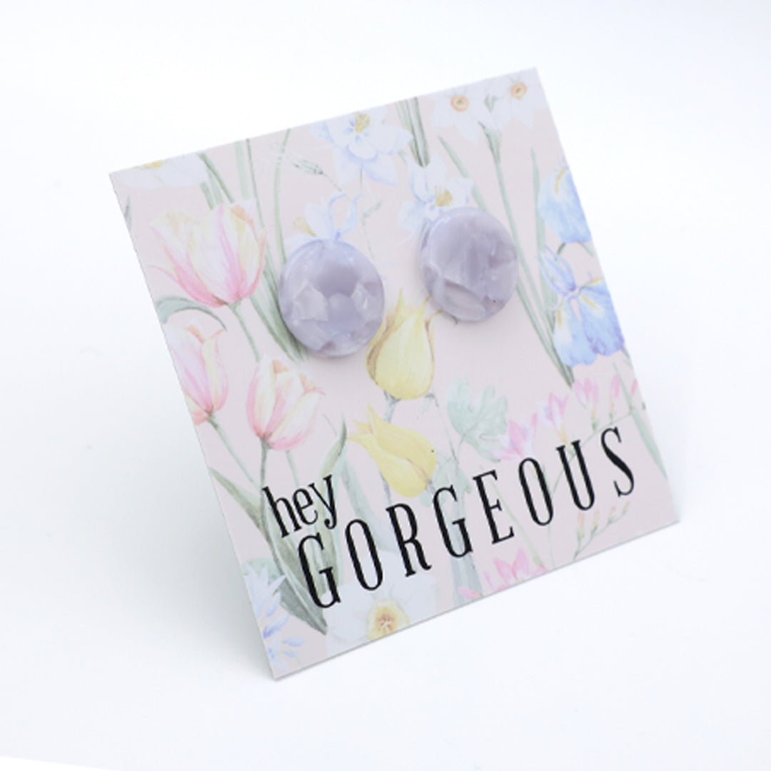 A pair of round, faceted lavender gemstone stud earrings displayed on a square floral backing card with the text 'hey GORGEOUS'.