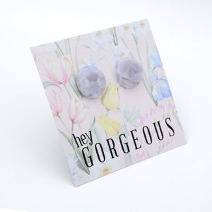 A pair of faceted lavender stud earrings displayed on a floral backing card that reads 'hey GORGEOUS' in black text.