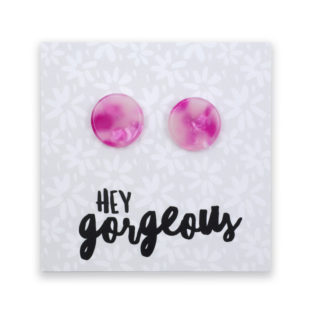 A pair of round stud earrings with a pink and purple marbled pattern, mounted on a white floral backing card that features the text 'HEY gorgeous' in black script.