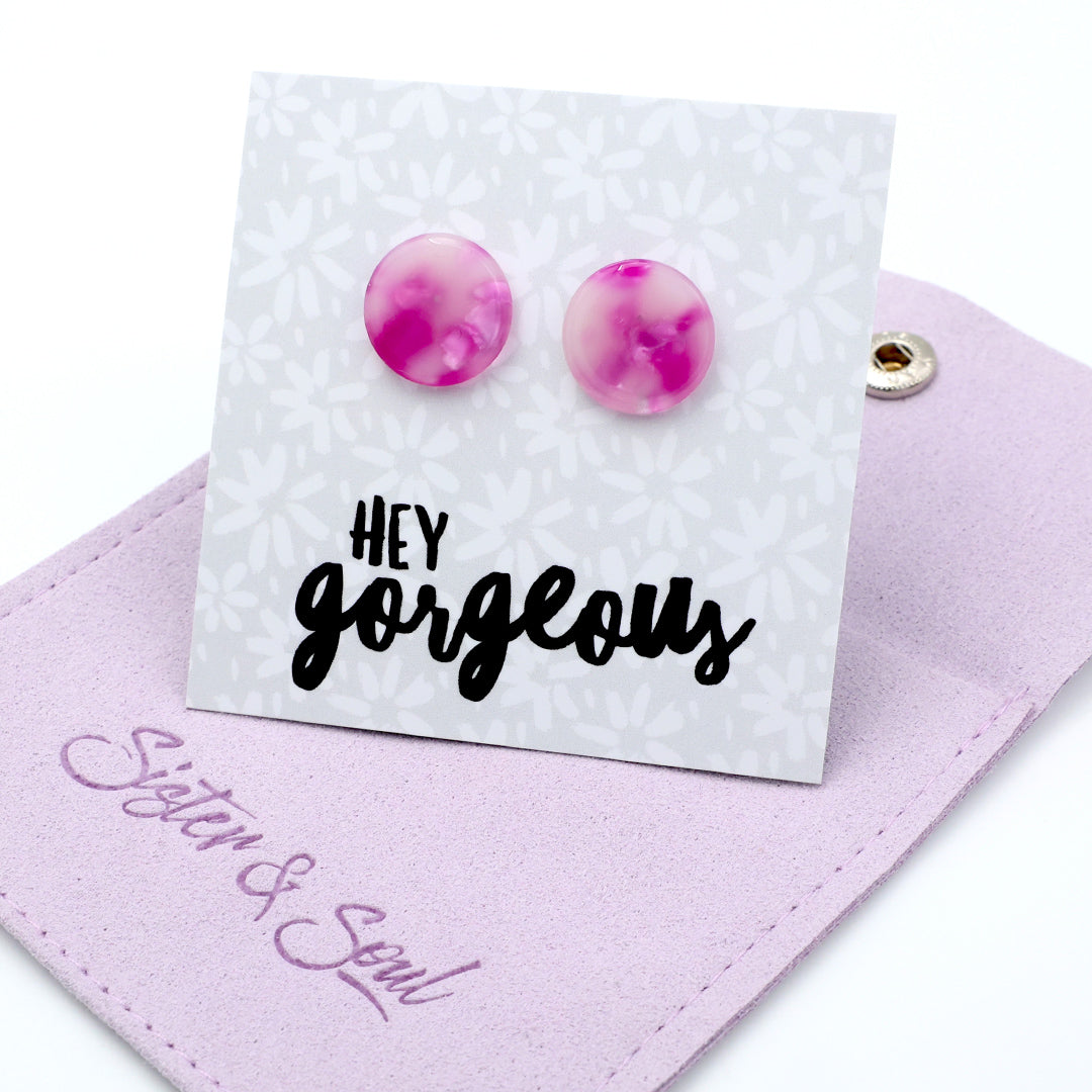 Pink and purple marbled round stud earrings displayed on a white floral backing card that reads 'HEY gorgeous', resting on a lavender fabric pouch with ' Sister & Soul'.