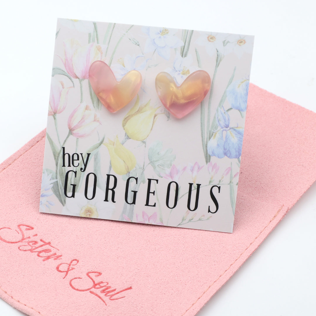 Heart-shaped earrings on a card with 'hey gorgeous' text on a pink pouch