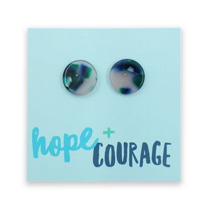A pair of round marbled stud earrings with green, blue, and white swirls, displayed on a light blue backing card that reads 'hope + COURAGE'.