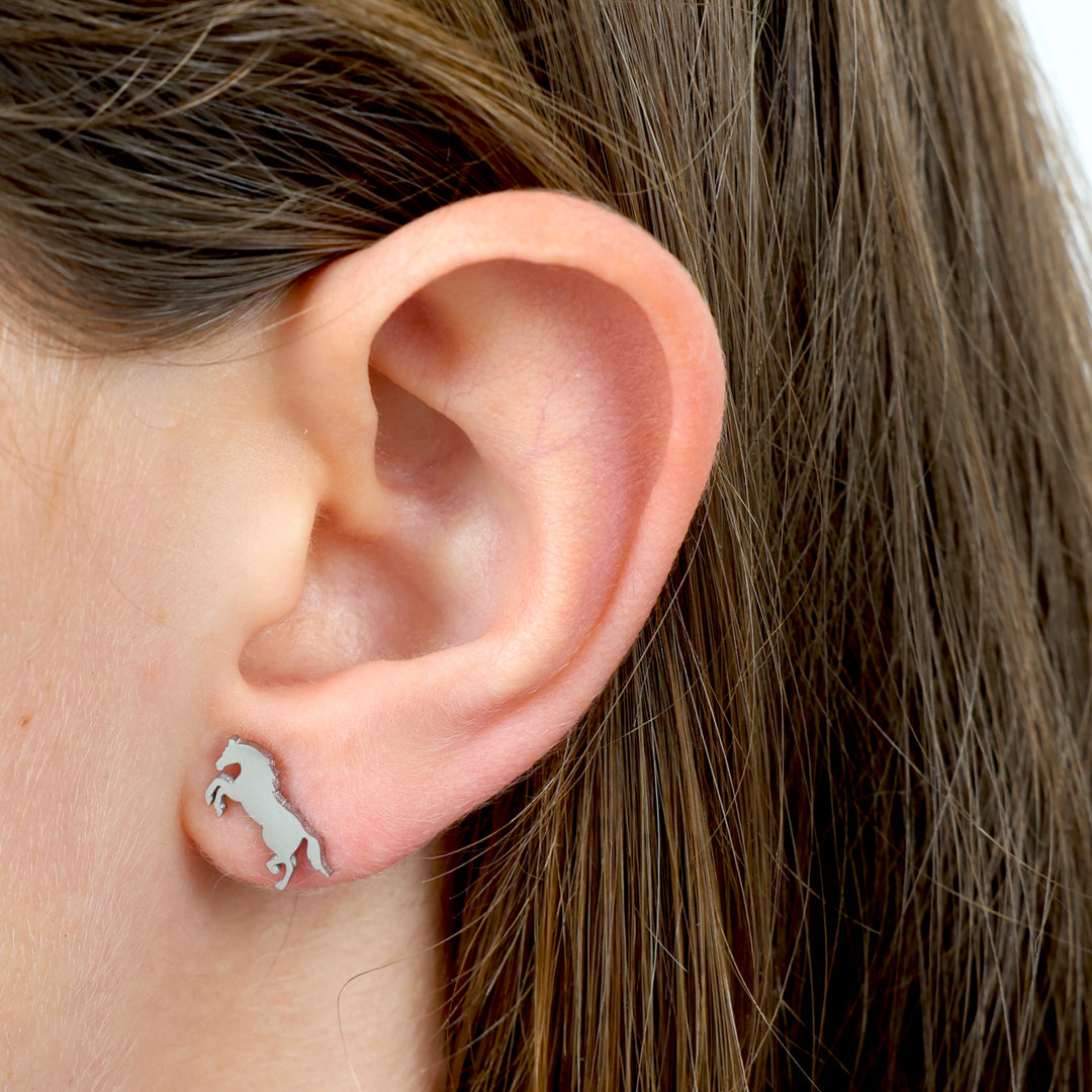 Close-up of an ear wearing a silver horse-shaped earring 