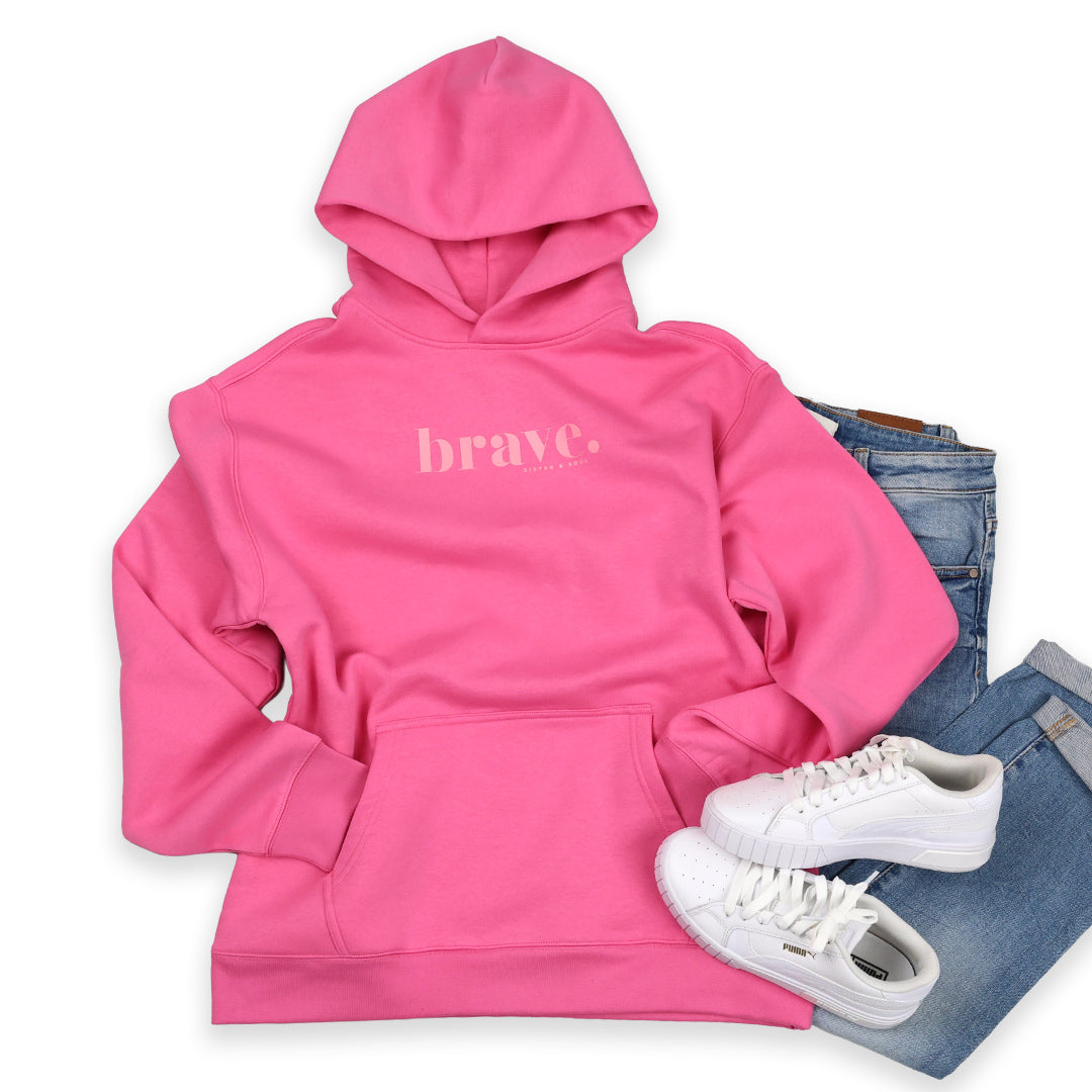 Pink hoodie with 'brave' text, white sneakers, and blue jeans on a white background