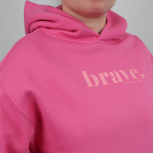 Pink hoodie with 'brave' text on a gray background