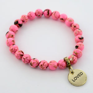 A collection of pink bead bracelets with vintage gold charms featuring words of courage and strength.