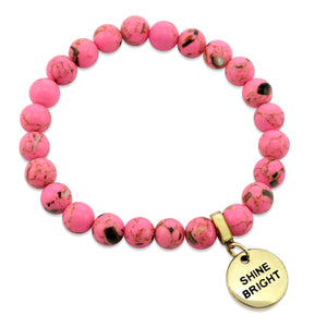 Pink beaded bracelet with a gold 'SHINE BRIGHT' charm on a white background
