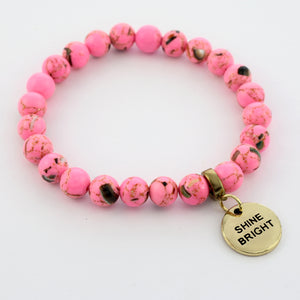 A collection of pink bead bracelets with vintage gold charms featuring words of courage and strength.