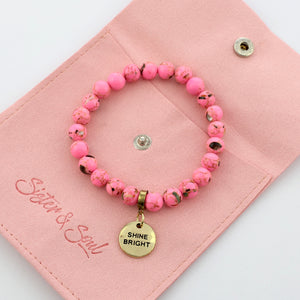 A collection of pink bead bracelets with vintage gold charms featuring words of courage and strength.