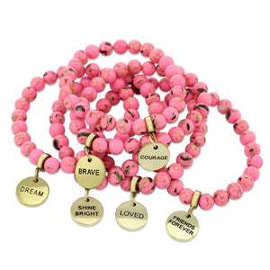 A collection of pink bead bracelets with vintage gold charms featuring words of courage and strength.