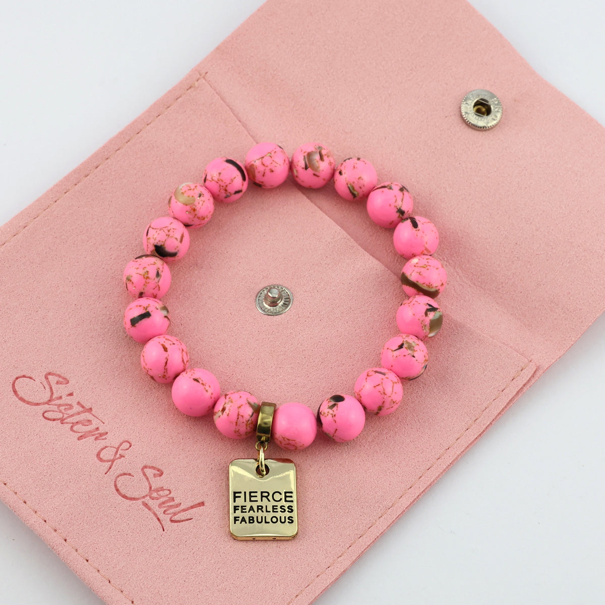 Pink beaded bracelet with a gold tag on a pink pouch