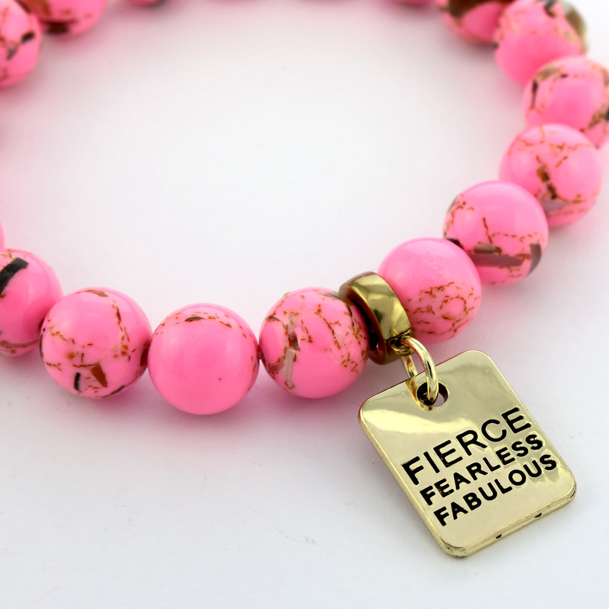 Pink beaded bracelet with a gold charm reading 'Fierce Fearless Fabulous' on a light background