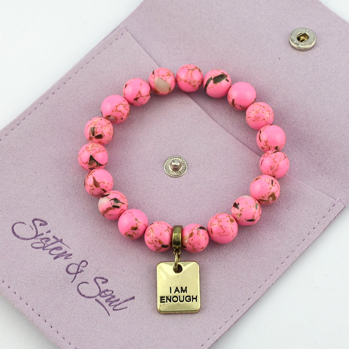 Pink beaded bracelet with 'I AM ENOUGH' charm on a purple pouch with 'Sister & Soul' branding.