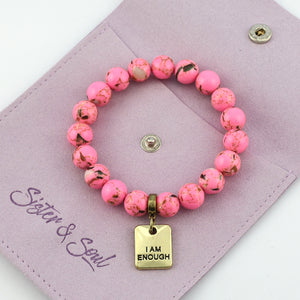 Pink beaded bracelet with 'I AM ENOUGH' charm on a purple pouch with 'Sister & Soul' branding.
