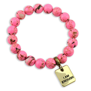 Pink beaded bracelet with a gold tag reading 'I AM ENOUGH' on a white background