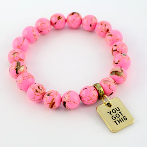 Pink beaded bracelet with a gold tag reading 'You Got This' on a white background