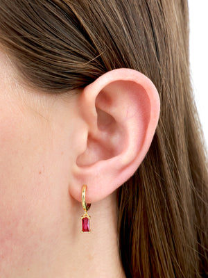 Gold hoop earring with deep pink feature stone in girls ear.